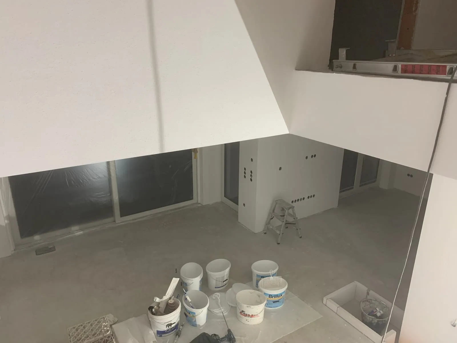 Wohnraum mit fertig gespachtelten Wänden und Decke, Farbeimer stehen für den Anstrich bereit