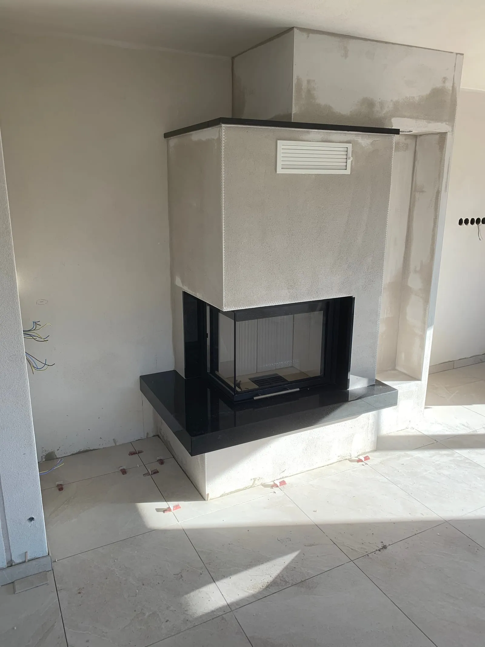 Moderner Eckkamin mit Glasscheibe und schwarzer Granitbank, fertig verputzt