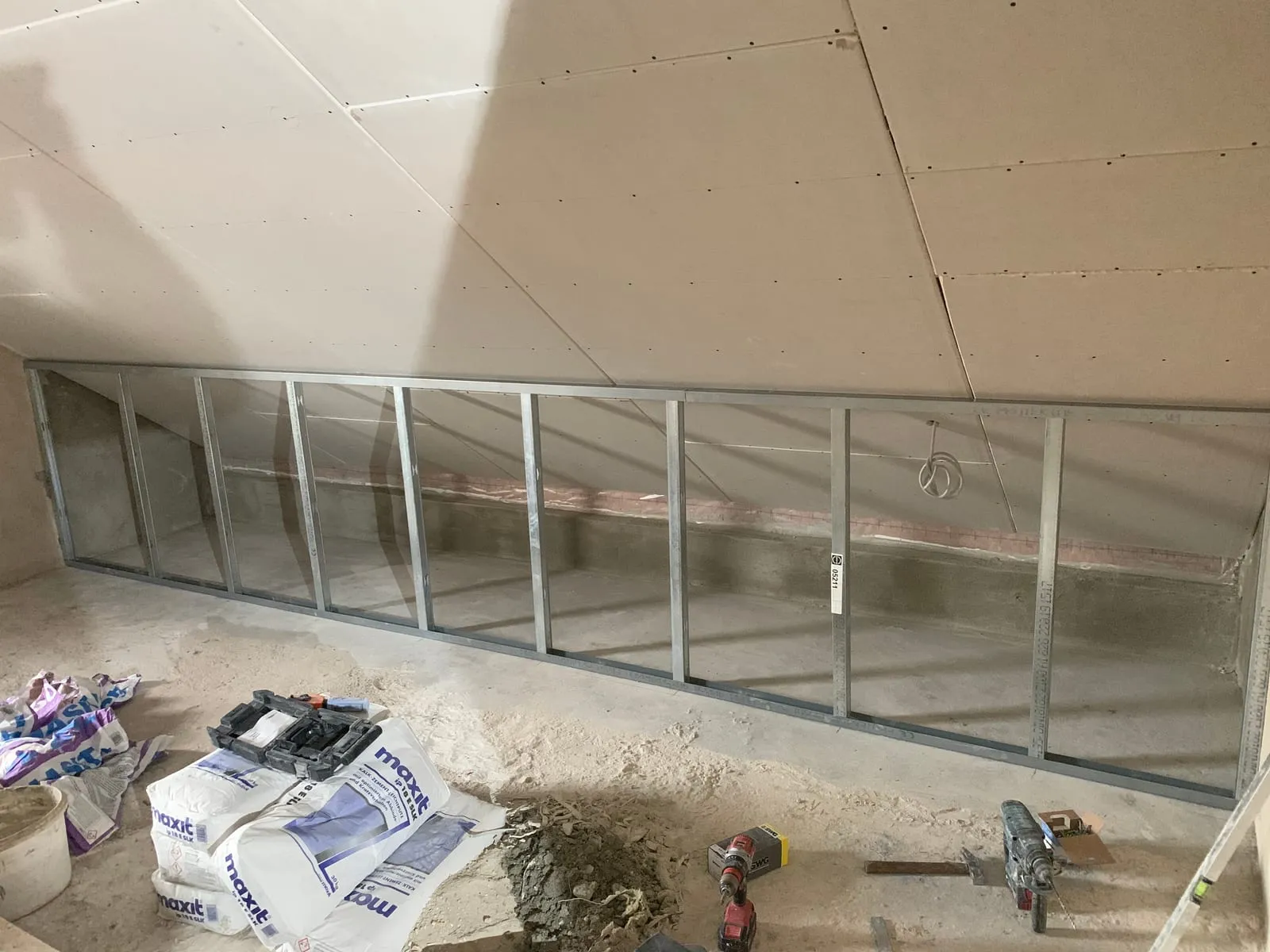 Langes Metallständerwerk einer Drempelwand unter der Dachschräge mit Werkzeug auf der Baustelle